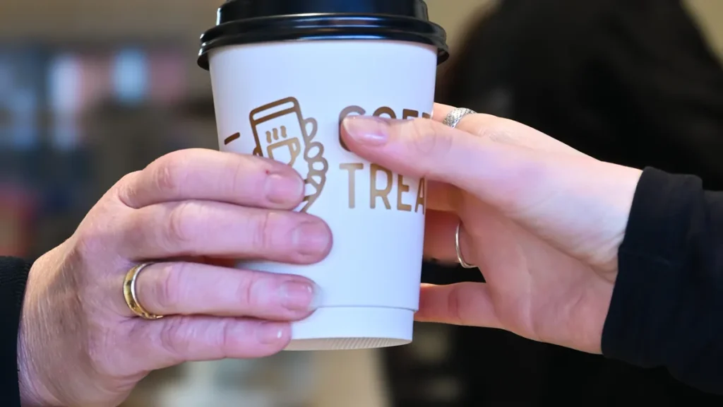A COFFEETREAT branded takeaway coffee cup being handed to a customer in store