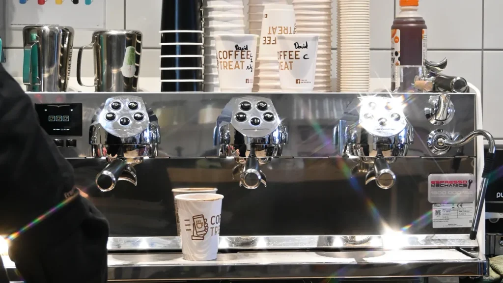 Commercial espresso machine at a COFFEETREAT store with branded takeaway cups stacked above