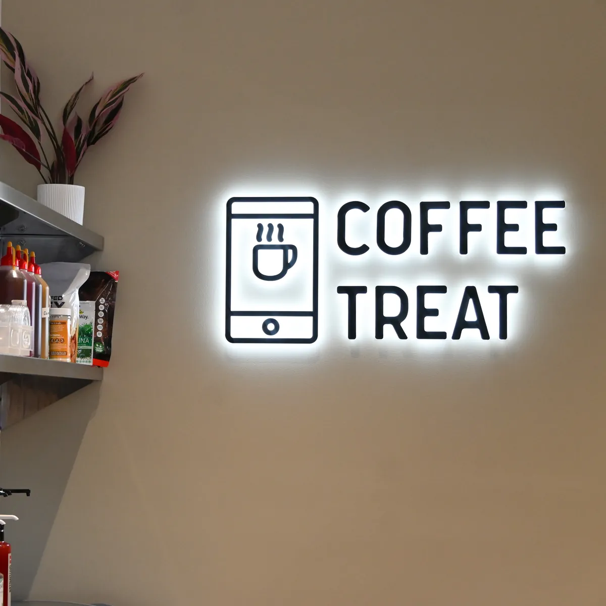 Illuminated COFFEETREAT neon sign on the wall inside a store, beside stocked shelves